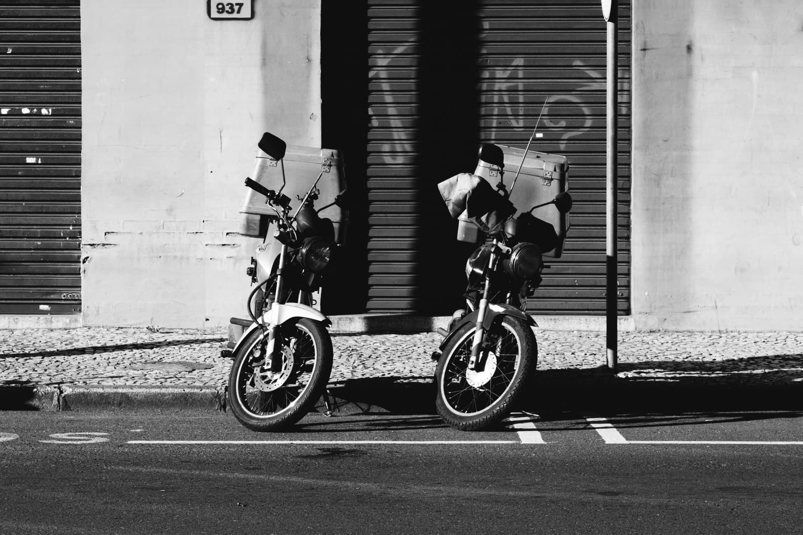 Dos motocicletas estacionadas en una calle de ciudad, en blanco y negro.
